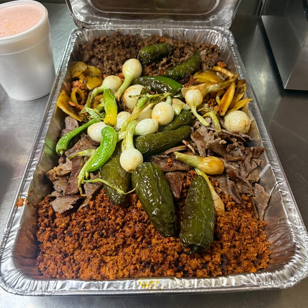 A large foil tray filled with various meats, grilled peppers, and onions, with a drink nearby.